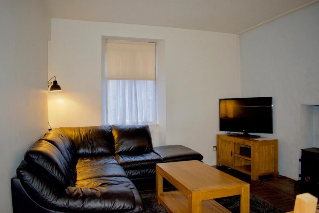 uma sala de estar com um sofá de couro preto e uma televisão em Central Apartment for the Fringe em Edinburgo