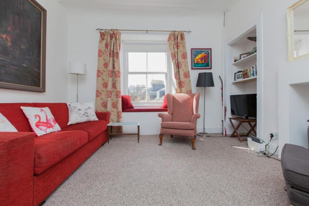 エディンバラにあるCharming City Centre Flat in Edinburghのリビングルーム(赤いソファ、椅子付)