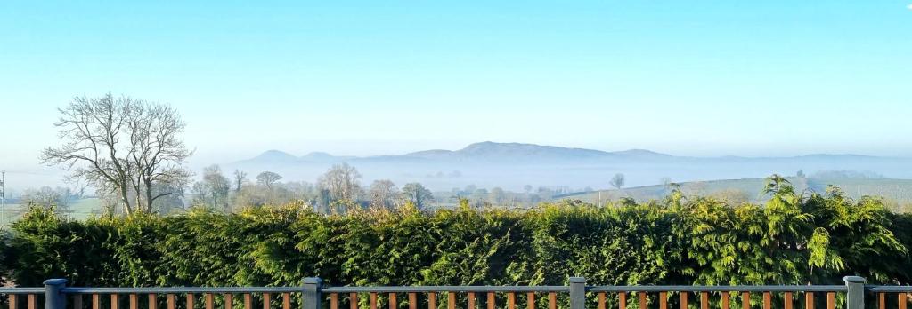 a fence in front of a hedge with mountains in the background at Yaseva Lodge, Stylish Country Retreat for 2, Hot Tub, Exceptional Views! in Carr