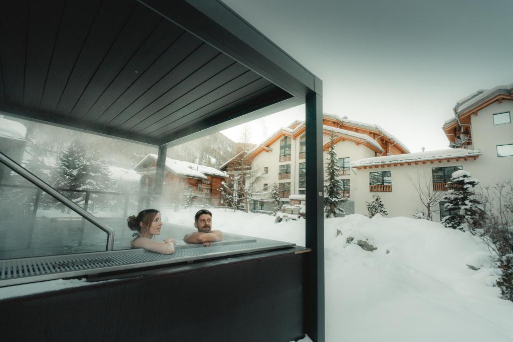 un hombre y una mujer en una bañera en la nieve en Zermatt Budget Rooms, en Zermatt