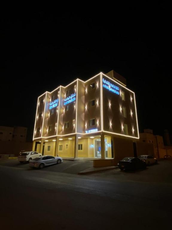 un edificio iluminado con coches estacionados en un estacionamiento en الواحة ان للشقق المخدومة, en Hotat bani tamim