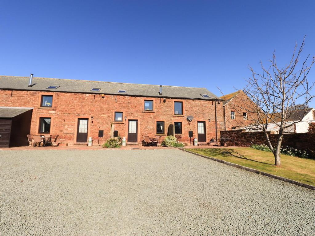 a large red brick building with a gravel driveway at Stable Cottage in Wigton