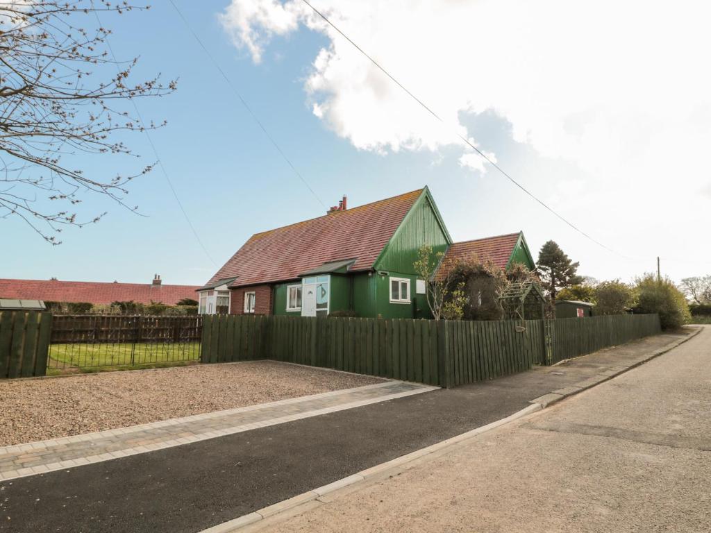 una casa detrás de una valla con una casa verde en Cra-na-ge, en Embleton