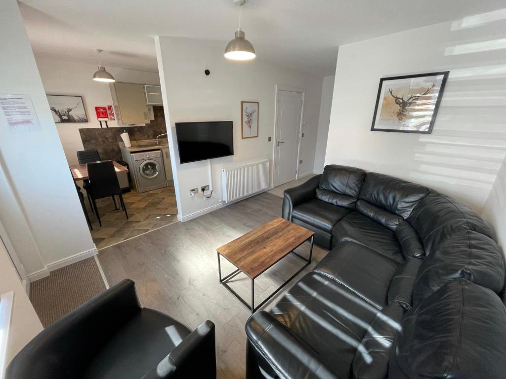 a living room with a black leather couch and a table at Foxglove Apartment in Inverness