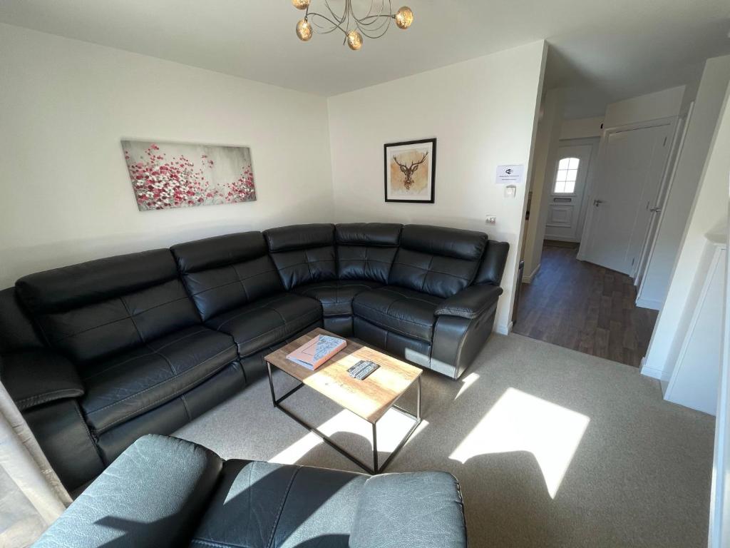 ein Wohnzimmer mit einem schwarzen Ledersofa und einem Tisch in der Unterkunft Gorsebank View in Inverness