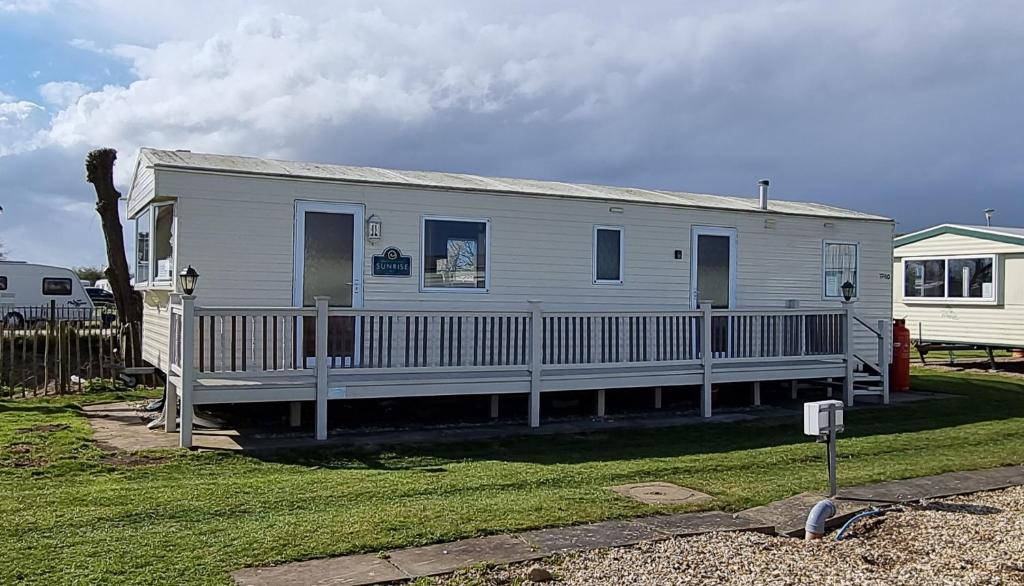 a white house with a porch and a fence at 8 BERTH CARAVAN TP60 ON THE GOLDEN PALM CHAPEL ST LEONARD in Chapel Saint Leonards