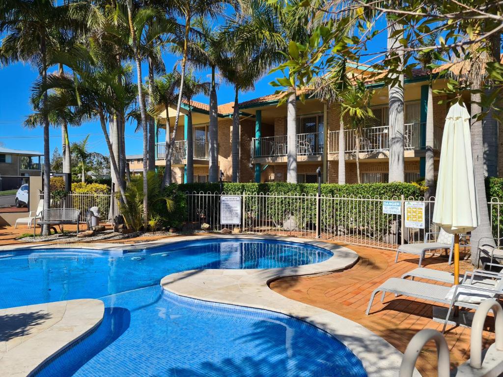 a swimming pool with palm trees and a house at Beaches Serviced Apartments in Nelson Bay