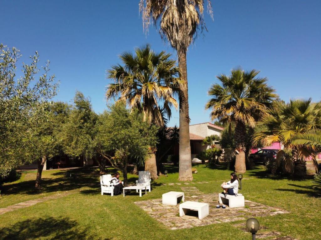 2 personnes assises sur des chaises dans un parc planté de palmiers dans l'établissement Residence Sa Pintadera, à Cabras