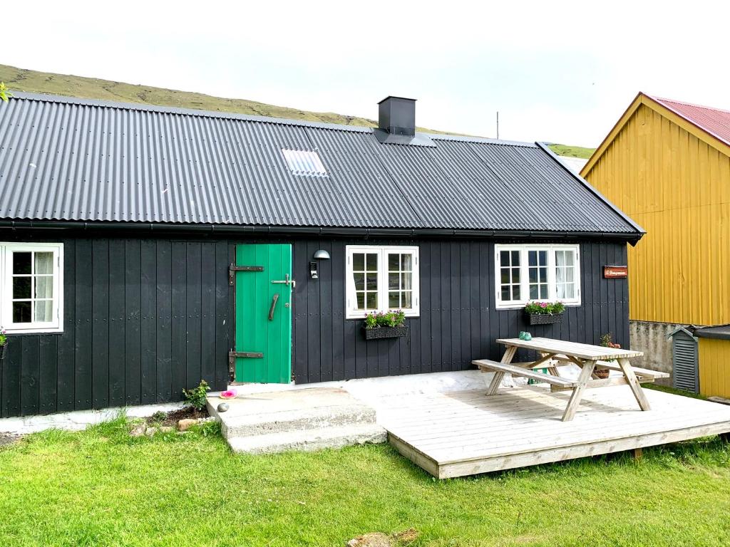 ein schwarzes Gebäude mit einer grünen Tür und einem Picknicktisch in der Unterkunft Charming old style shanty in Hvalba
