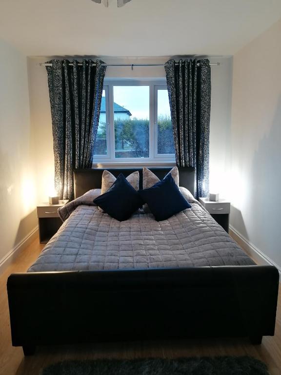a bed with blue pillows in a bedroom with a window at Chota Gher Apartment in Widnes