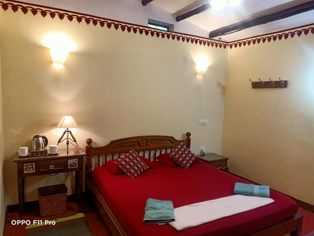 una camera con letto rosso, tavolo e lampada di Namaste Yoga Farm a Gokarna