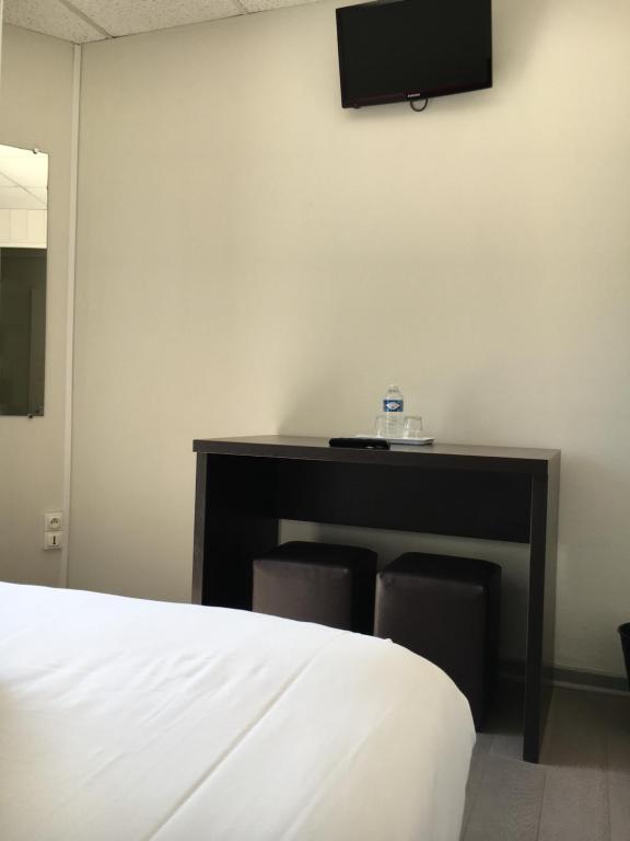 a bedroom with a bed and a desk with a tv on the wall at Les Bains Boyardville - Hôtel et Restaurant in Boyard-Ville