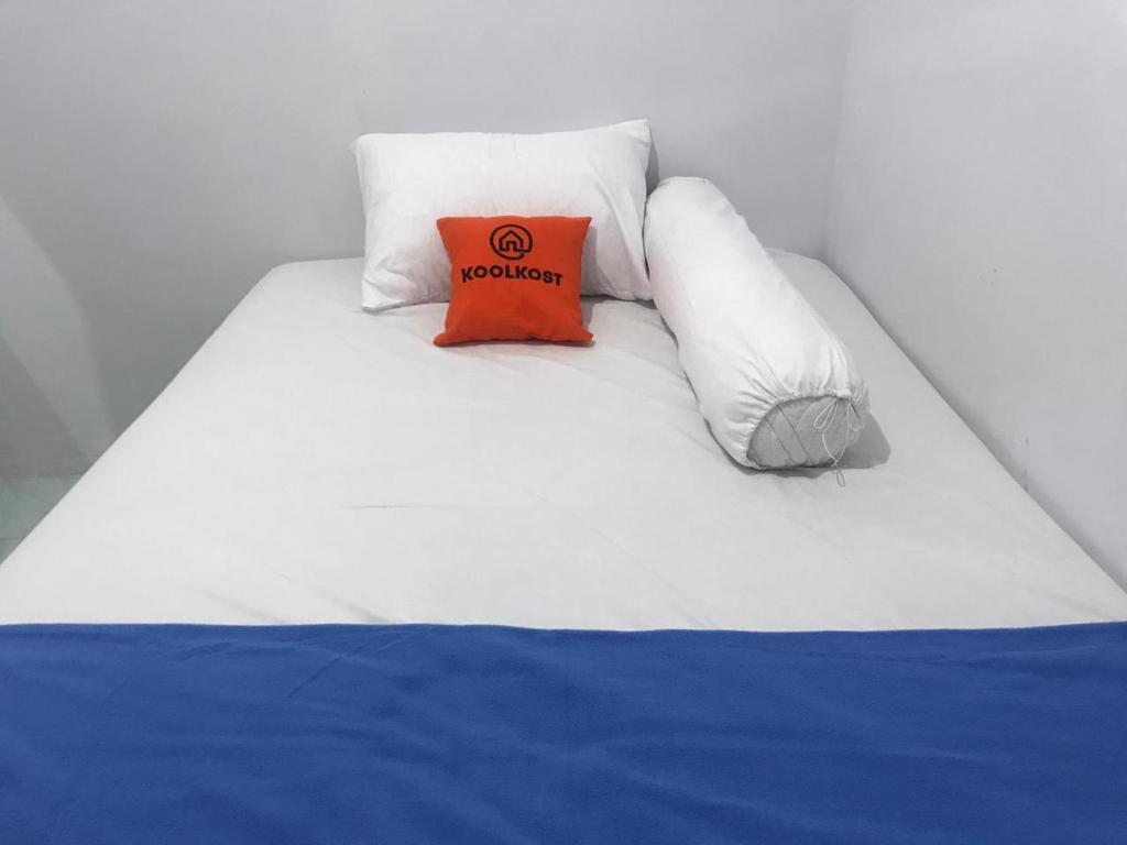 a white bed with an orange pillow on it at KoolKost Syariah near Pelabuhan Tanjung Priok (Minimum Stay 6 Nights) in Jakarta