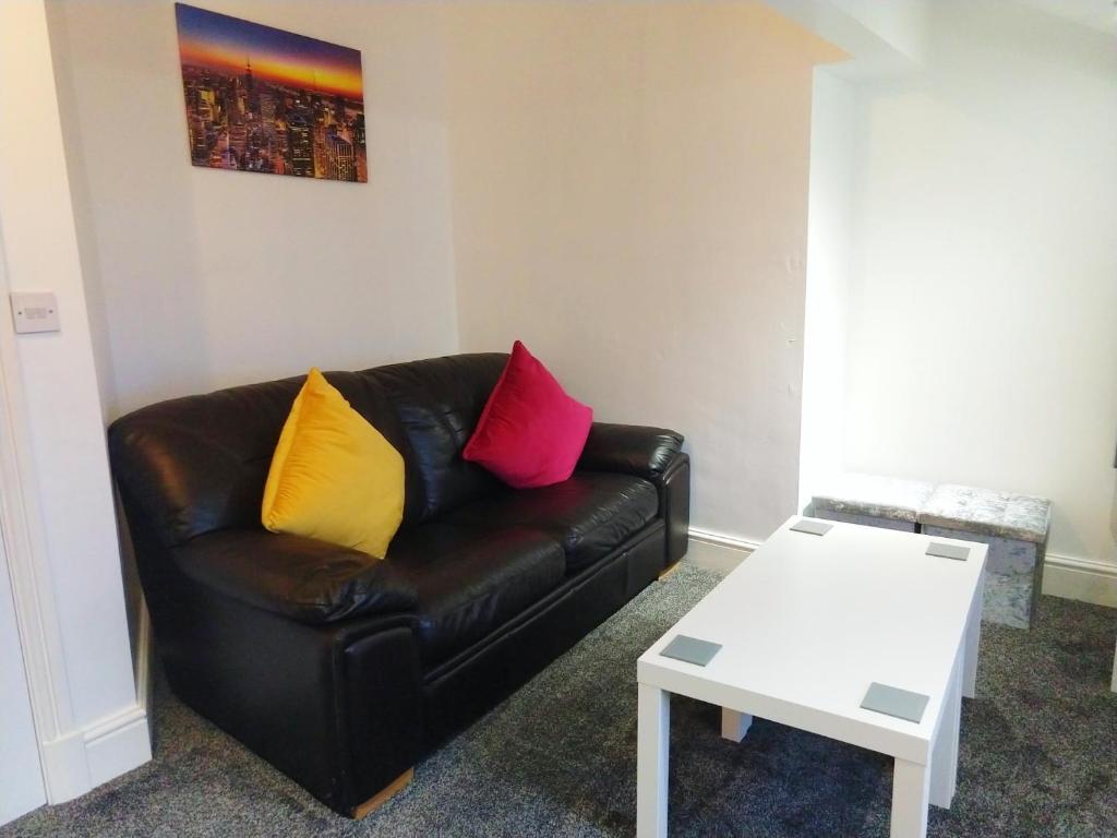 a living room with a black leather couch with colorful pillows at Derwent Street Apartment 3 - Self Contained - 2 Bed Self Catering Apartment in Workington