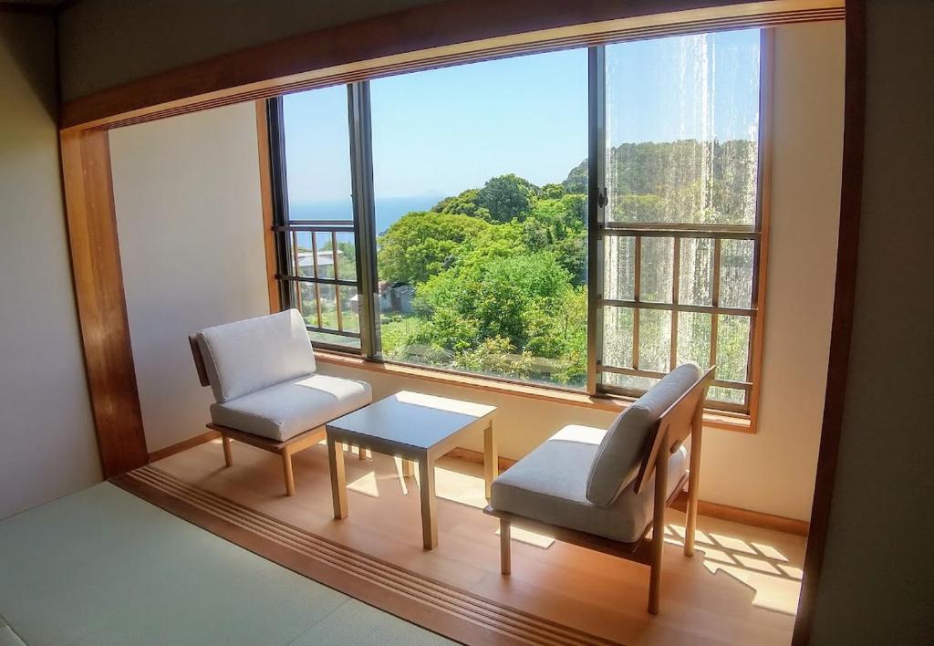 a room with two chairs and a table and a large window at FUTO HOUSE -Ippon no Enpitsu- in Ito