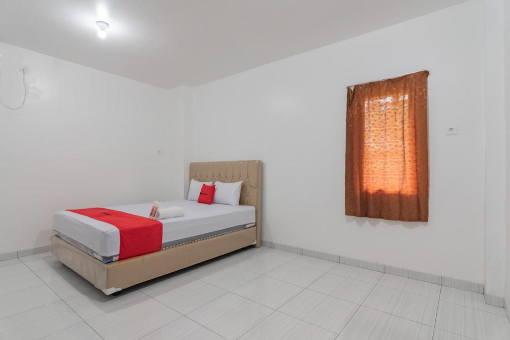 una camera da letto con un letto con una coperta rossa e una finestra di RedDoorz at Vall Guest House Balikpapan a Balikpapan