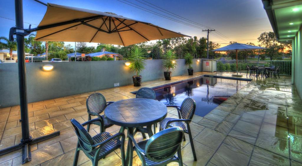 a table with chairs and an umbrella next to a pool at Chinchilla Motor Inn in Chinchilla