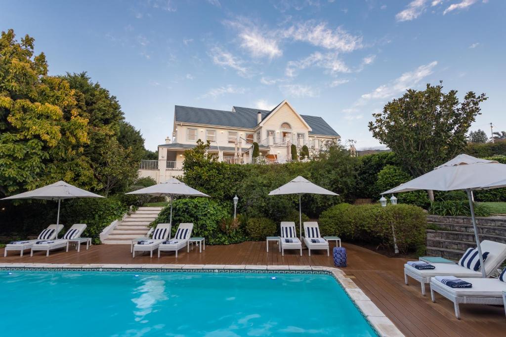a pool with chairs and umbrellas in front of a house at The Light House Boutique Suites in Paarl