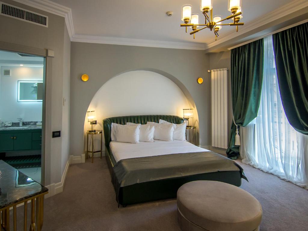 Green upholstered bed with arched alcove, bedside lamps, round wall sconces, velvet curtains and en-suite bathroom at Hotel Lido by Phoenicia in Bucharest