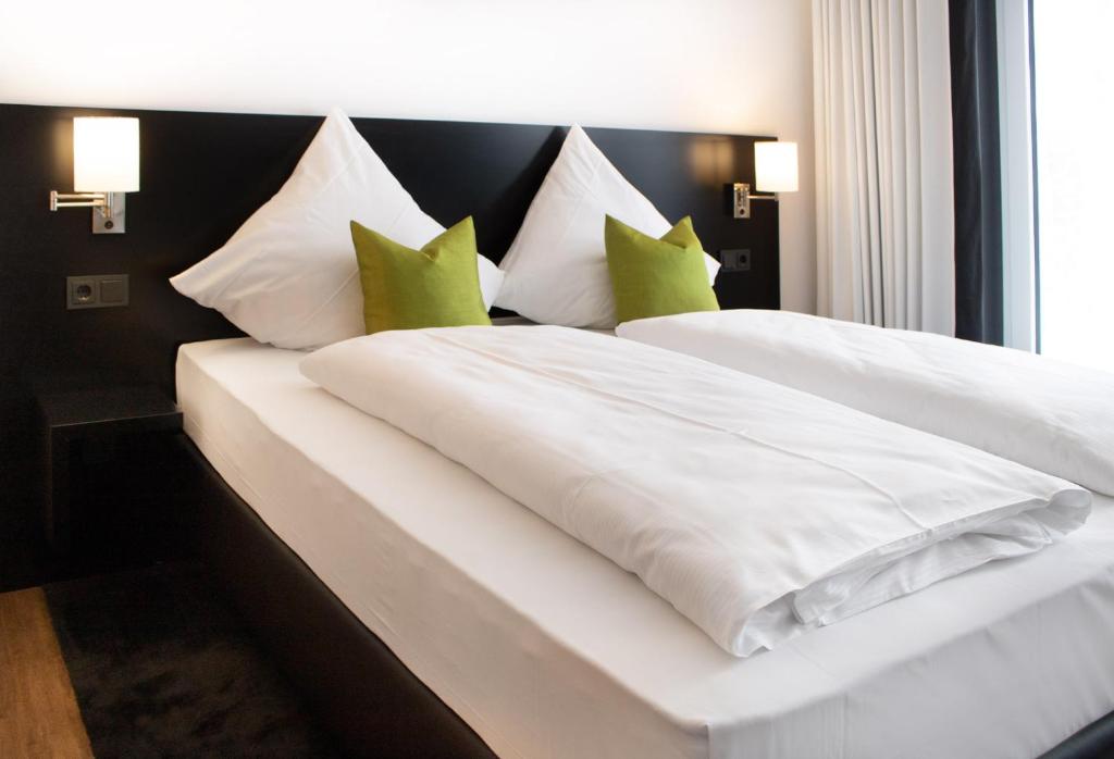 1 dormitorio con cama blanca y almohadas verdes en NHI Hotel by WMM Hotels en Neuhaus am Inn