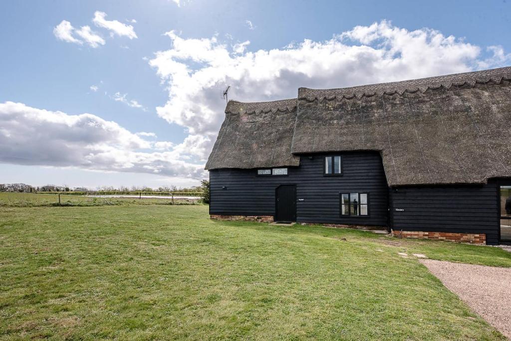 a black barn with a thatched roof in a field at The Hayloft Valley Farm Barns Snape Air Manage Suffolk in Saxmundham