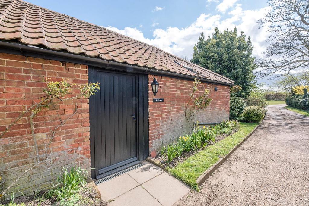 uma casa de tijolos com uma porta preta e uma entrada em The Stables Valley Farm Barns Snape Air Manage Suffolk em Saxmundham
