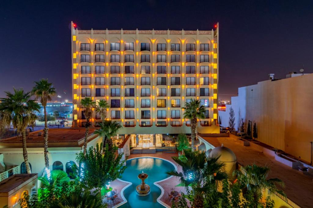 a hotel with a pool and palm trees at night at Hotel Lucerna Ciudad Juarez in Ciudad Juárez