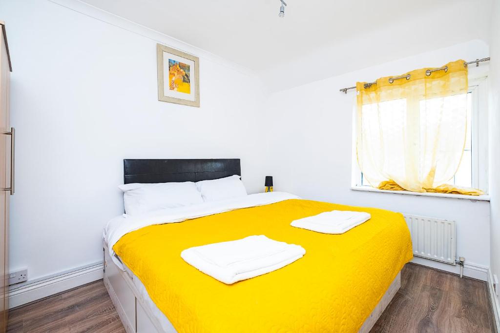 a bedroom with a yellow bed with two towels on it at 4 Bedrooms Self Catering Dagenham House, Free Wifi & Netfix in Dagenham