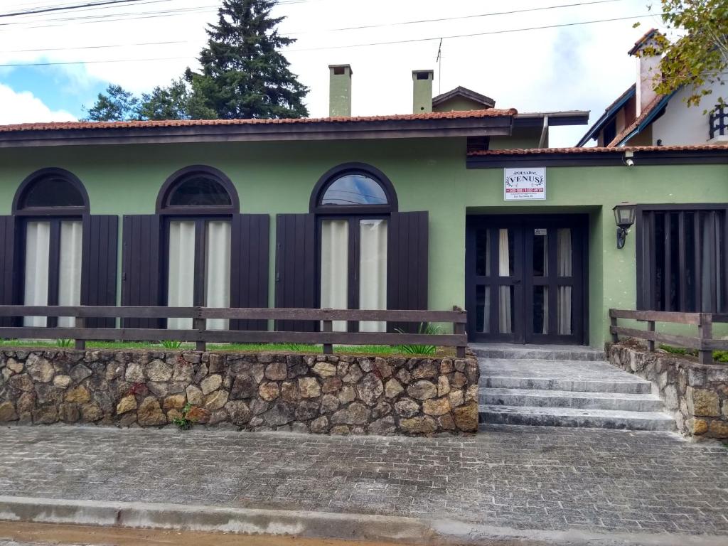 una casa verde con una pared de piedra en Pousada Vênus en Monte Verde