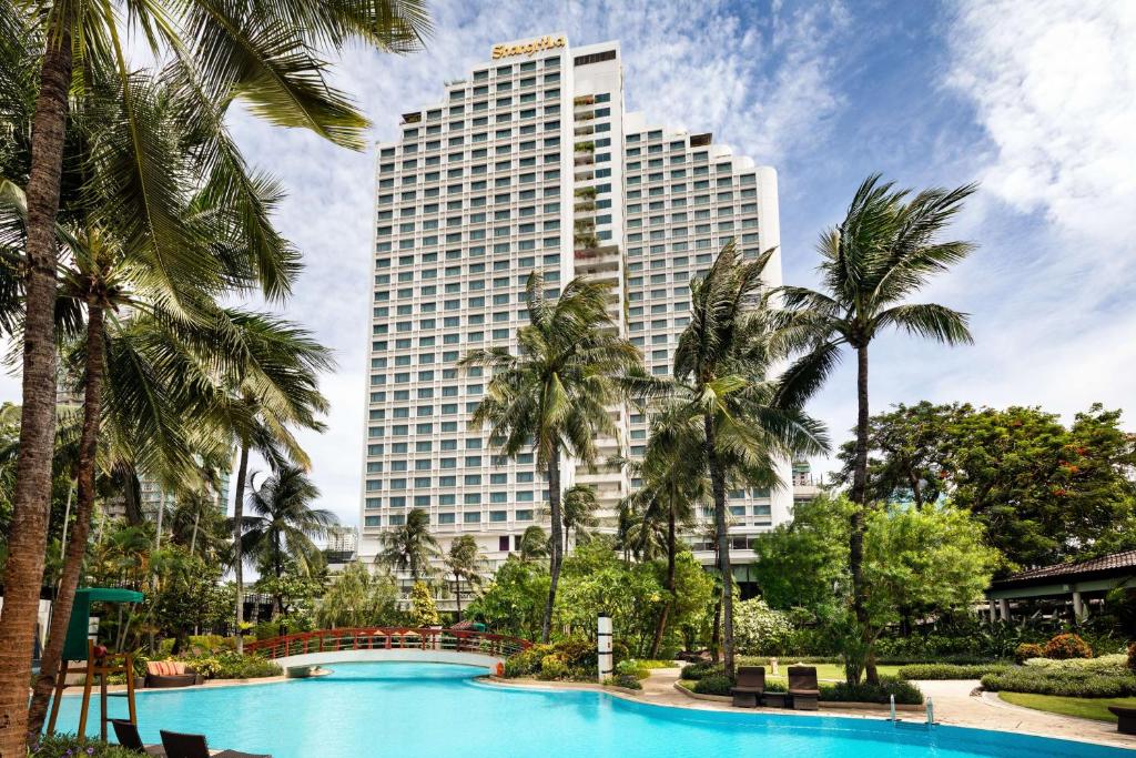 a tall building with palm trees in front of a pool at Shangri-La Jakarta in Jakarta