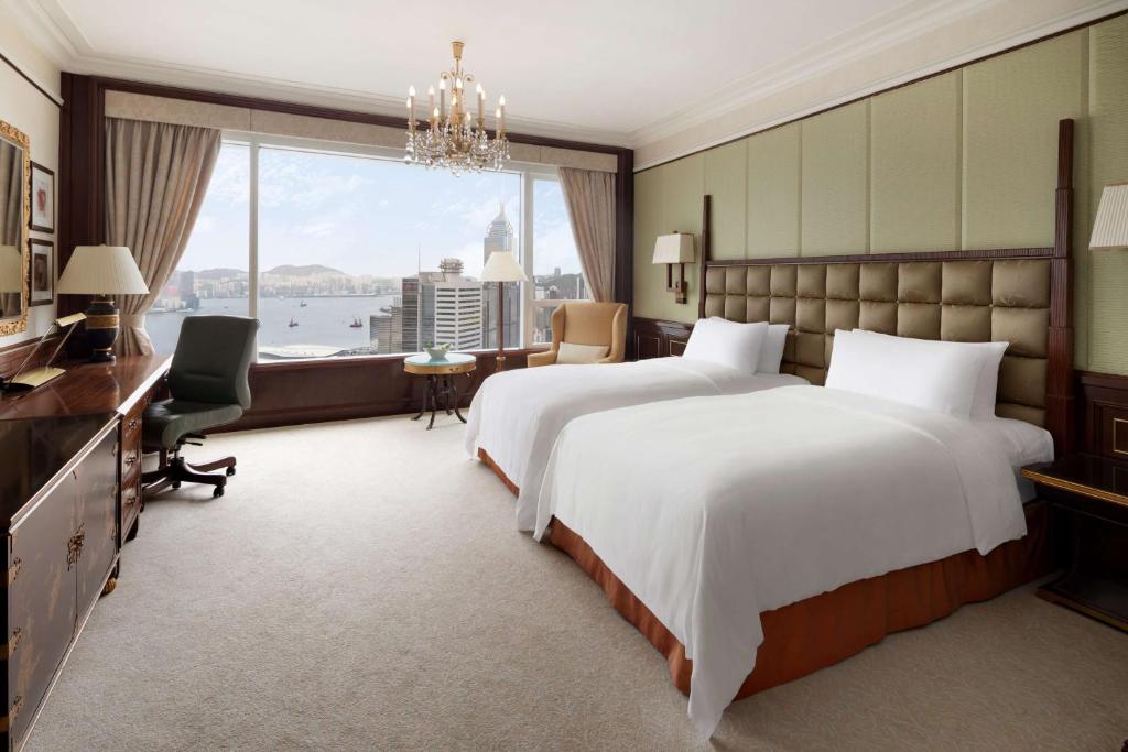 a bedroom with two beds and a desk and a window at Island Shangri-La, Hong Kong in Hong Kong