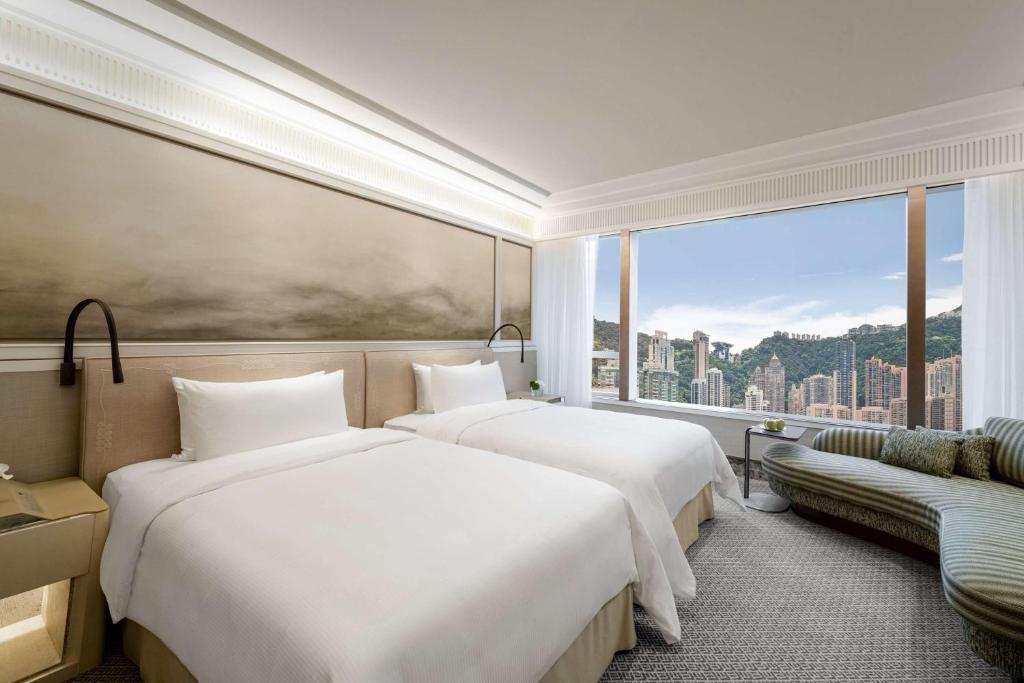 two beds in a hotel room with a large window at Island Shangri-La, Hong Kong in Hong Kong