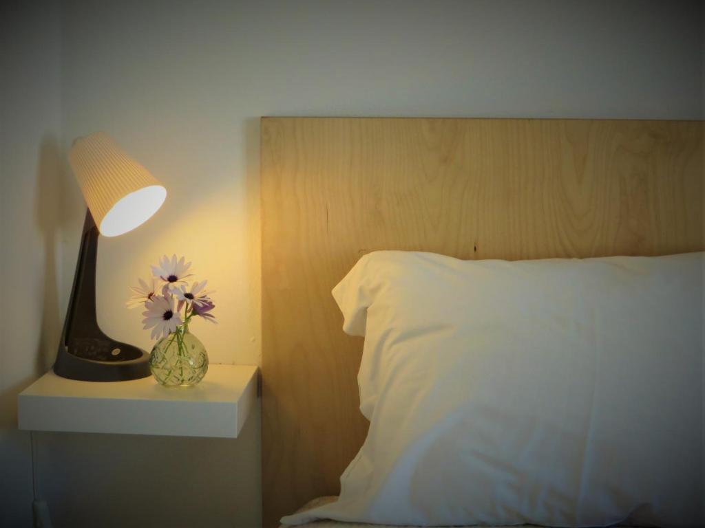 a bed with a lamp and a vase with flowers in it at HAUS NUNES by Stay in Alentejo in Vila Nova de Milfontes