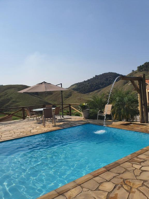 a swimming pool with a table and an umbrella at Pousada Recanto da Lunane in Barra do Piraí