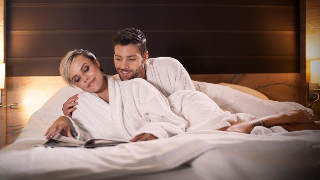 un hombre y una mujer acostados en la cama leyendo un libro en Hotel & Restaurant Waldblick, en Pulsnitz