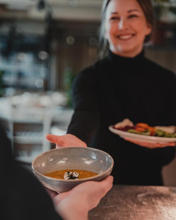 a woman holding a bowl of soup with a plate of food at VALO Hotel & Work Helsinki in Helsinki