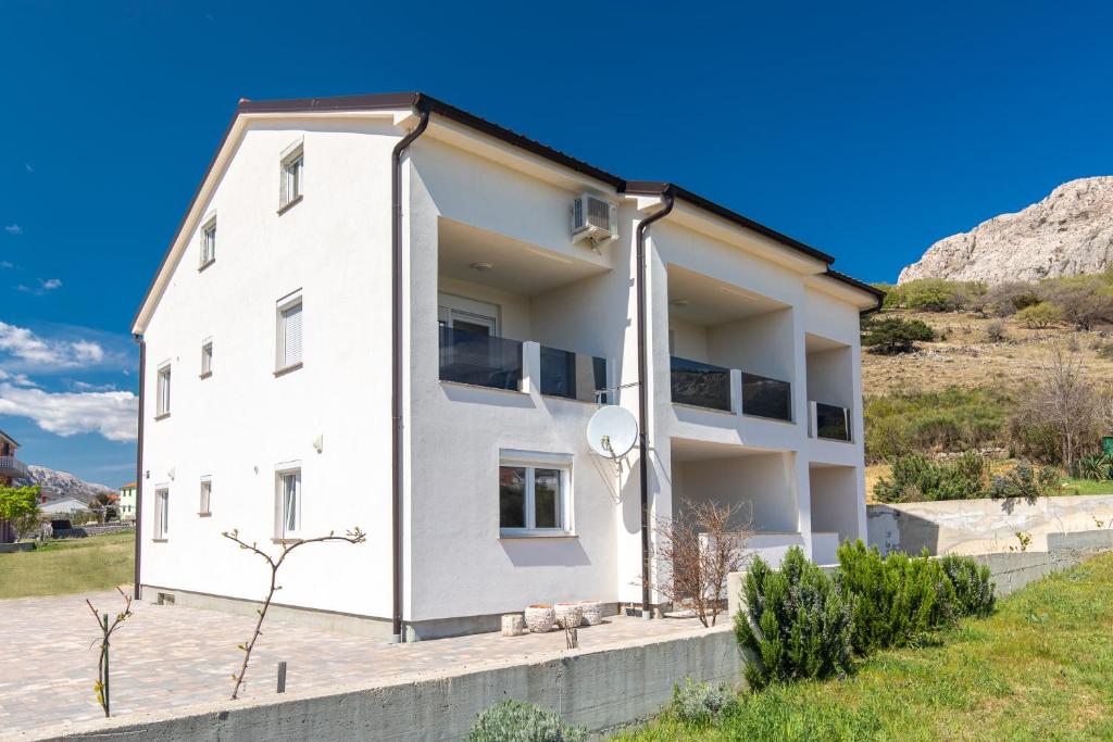 ein weißes Haus mit einem Hügel im Hintergrund in der Unterkunft Apartments Augustinovic in Baška