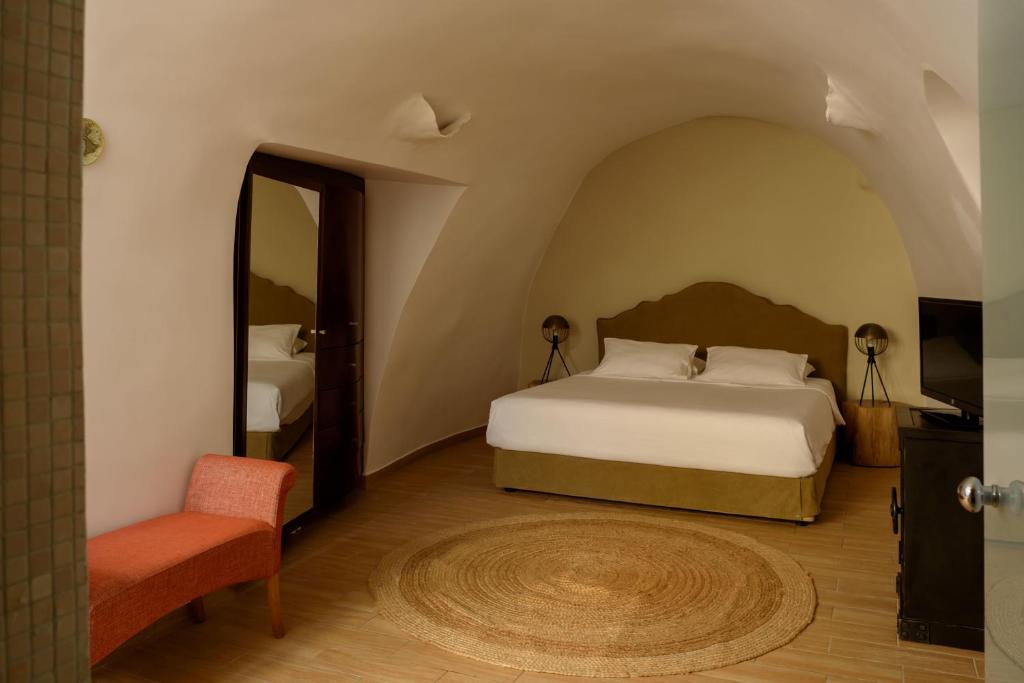 a bedroom with a bed and a chair and a mirror at Suite Home Santorini in Fira