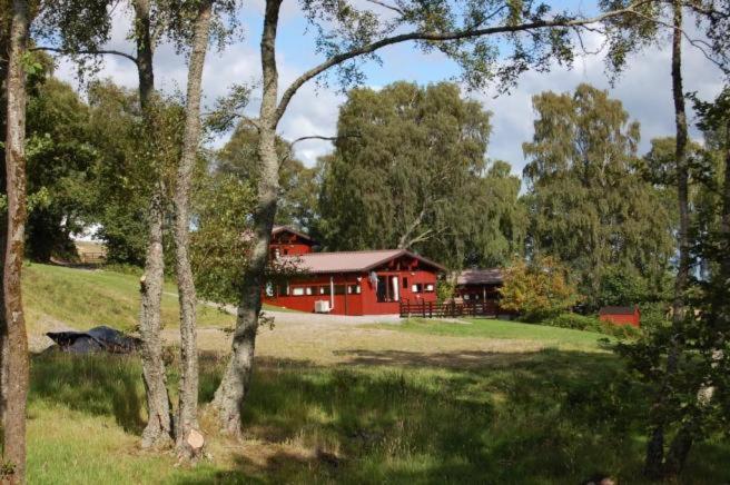 ein rotes Haus inmitten eines Feldes mit Bäumen in der Unterkunft Highland Lodge in Kilmorack