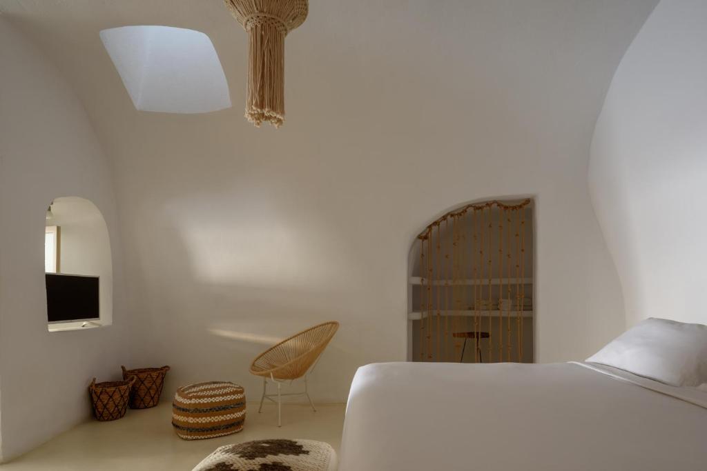 a white bedroom with a bed and a chair at Suite Home Santorini in Fira