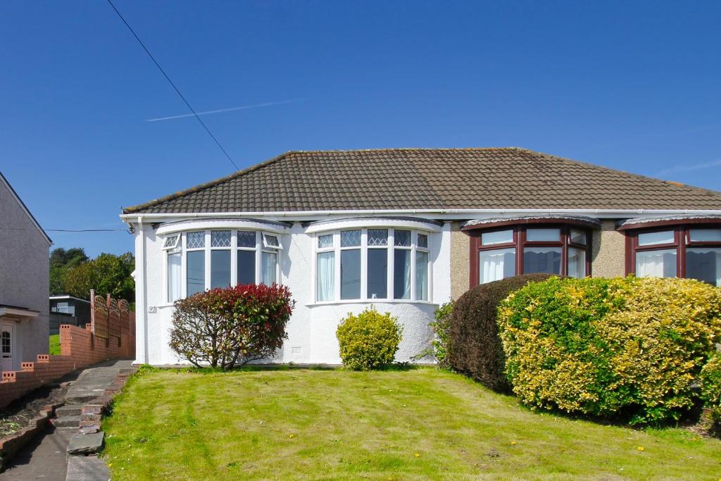 een wit huis met ramen en struiken bij Blue Rose Cottage in Burry Port