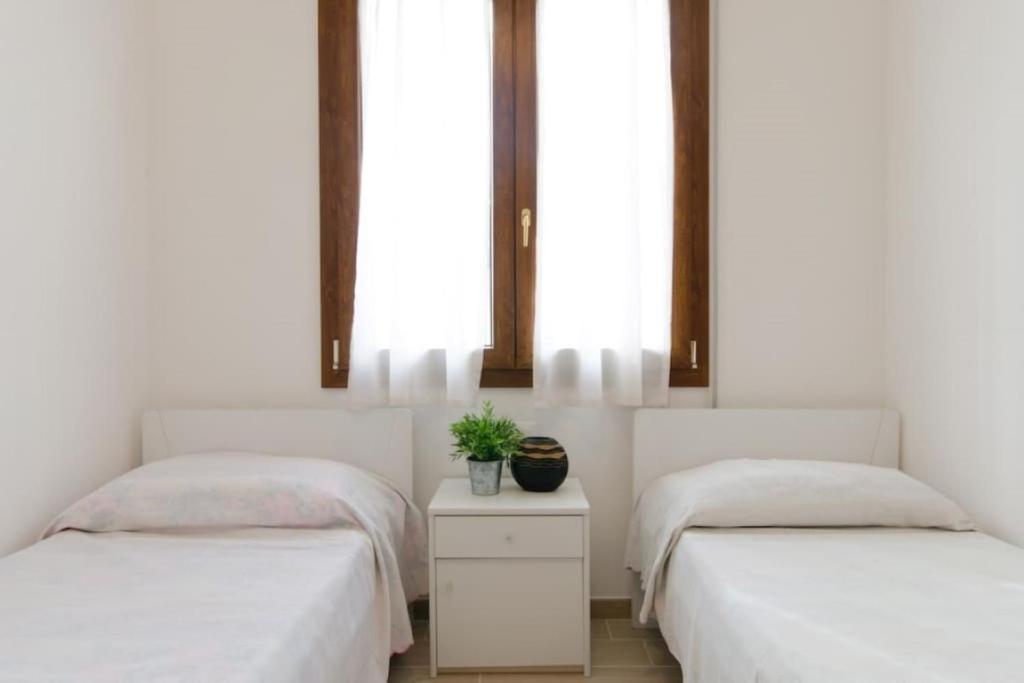 2 camas con sábanas blancas y una planta en una habitación en Villa Giuri, en Lido di Pomposa