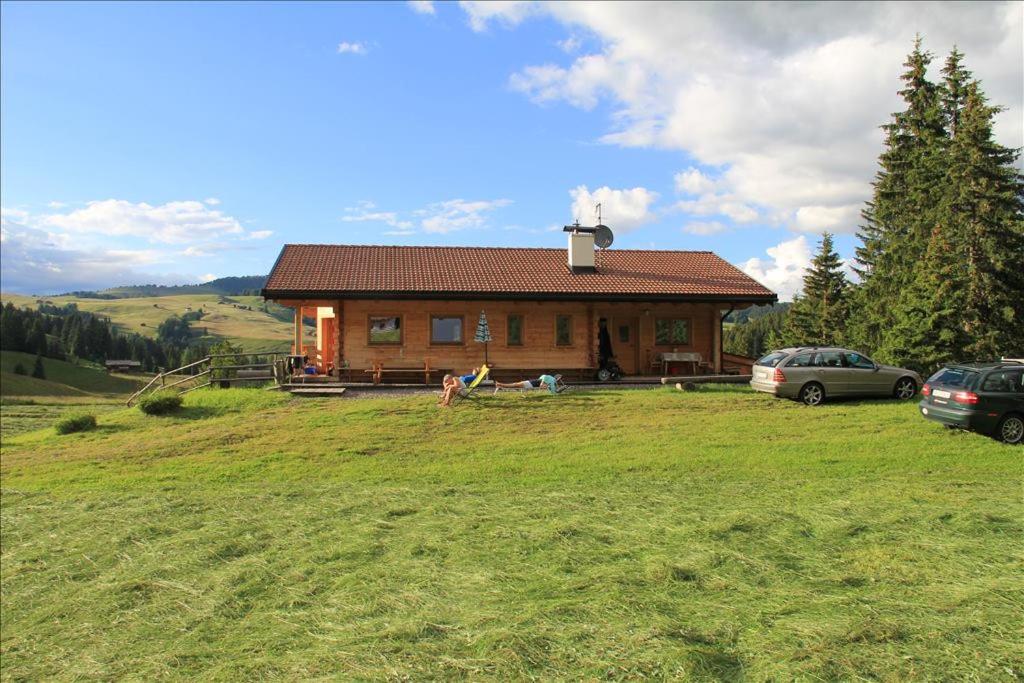 a small house in a field with cars parked in front of it at Almhütte Tirler Schweige in Alpe di Siusi