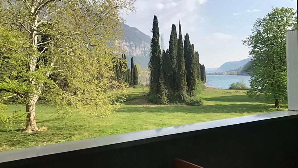 a window view of a park with trees and a lake at La casa sul lago in Maroggia