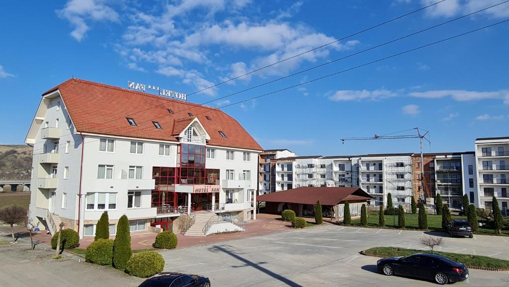 a large white building with a red roof in a parking lot at Hotel FAN Sebes in Sebeş