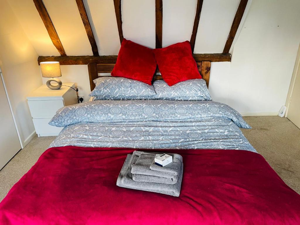 a bed with red pillows and a red blanket at Charming Town Centre Character Cottage With Parking in Stowmarket