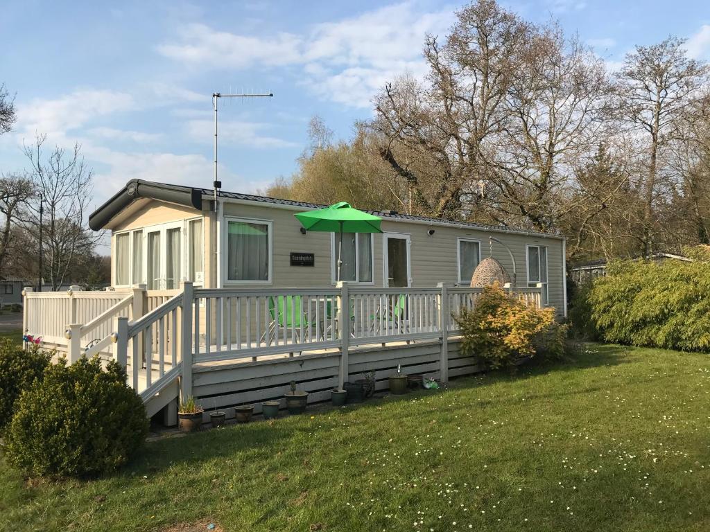 a small house with a green umbrella on a deck at Poppy at Oakdene Forest Park in Ringwood