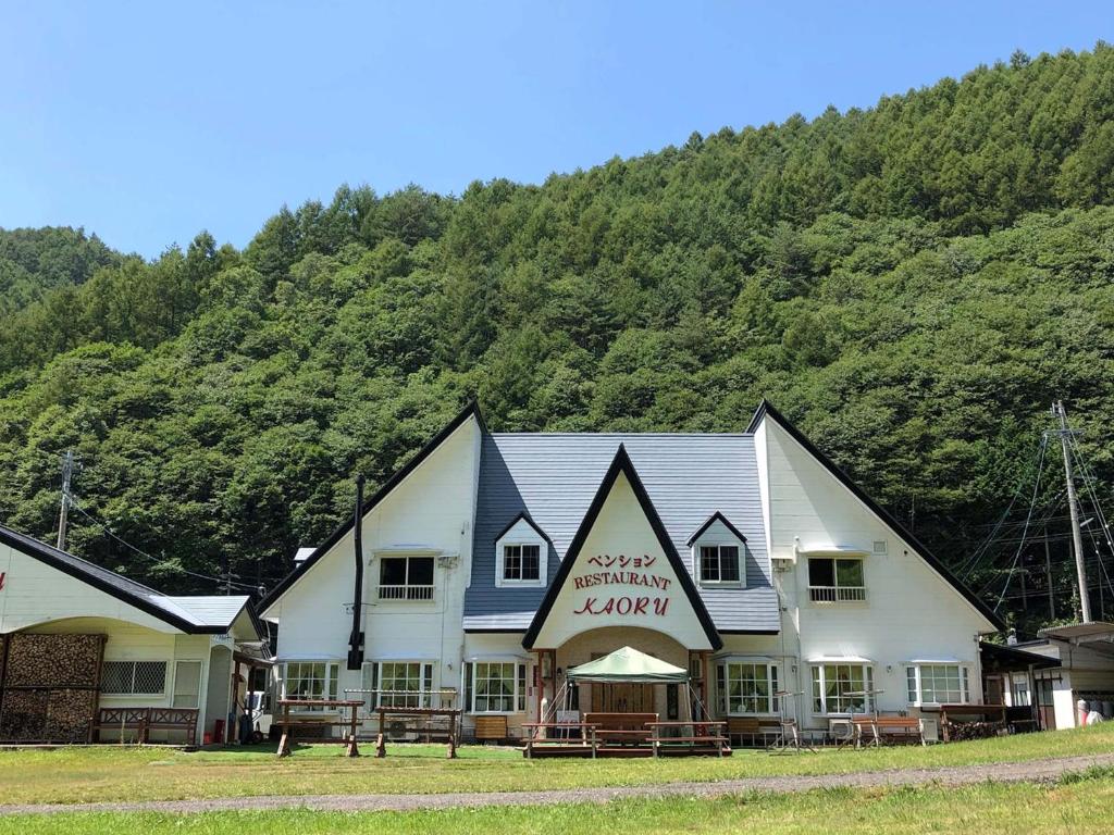 a large white building with a mountain in the background at Pension Kaoru in Kiso