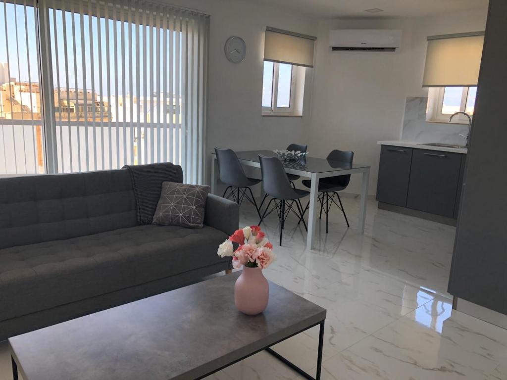 a living room with a couch and a vase with flowers on a table at Bugibba Sunrise View Modern Apartment in St Paul's Bay