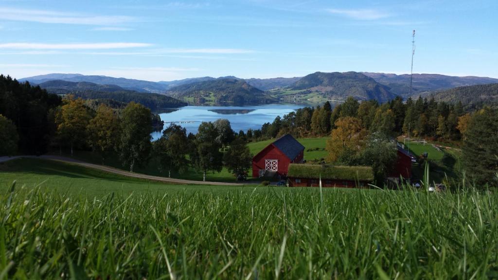 a red barn in a field with a lake and mountains at Yttervik gard in Steinkjer